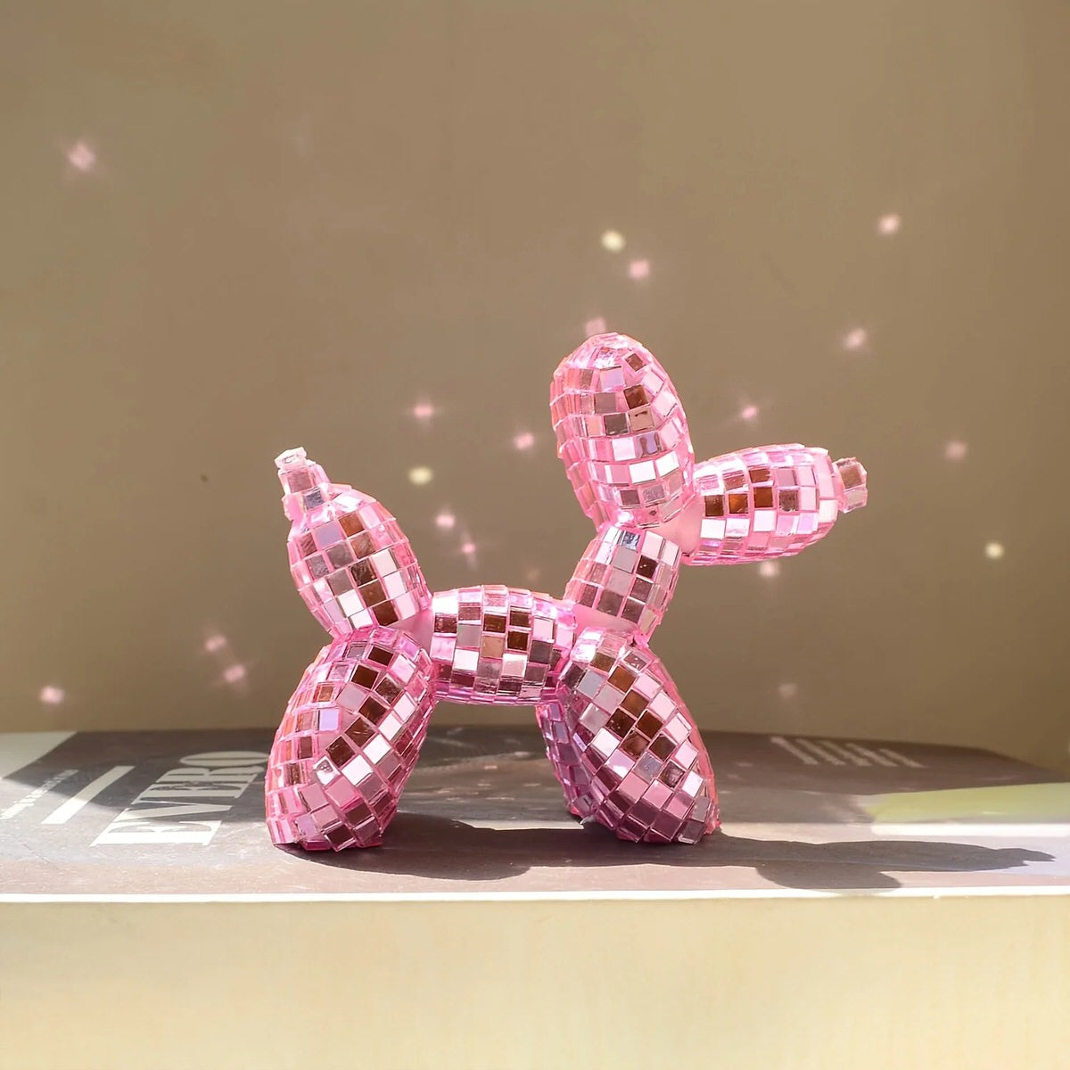 Small mirrored balloon dog decorative sculpture in silver and pink mosaic finish reflecting sunlight on a tabletop.