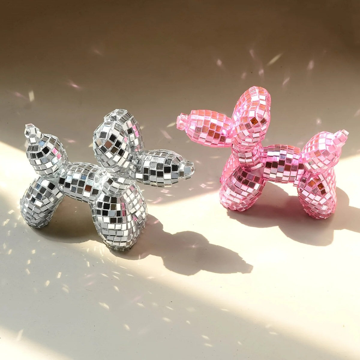Small mirrored balloon dog decorative sculpture in silver and pink mosaic finish reflecting sunlight on a tabletop.