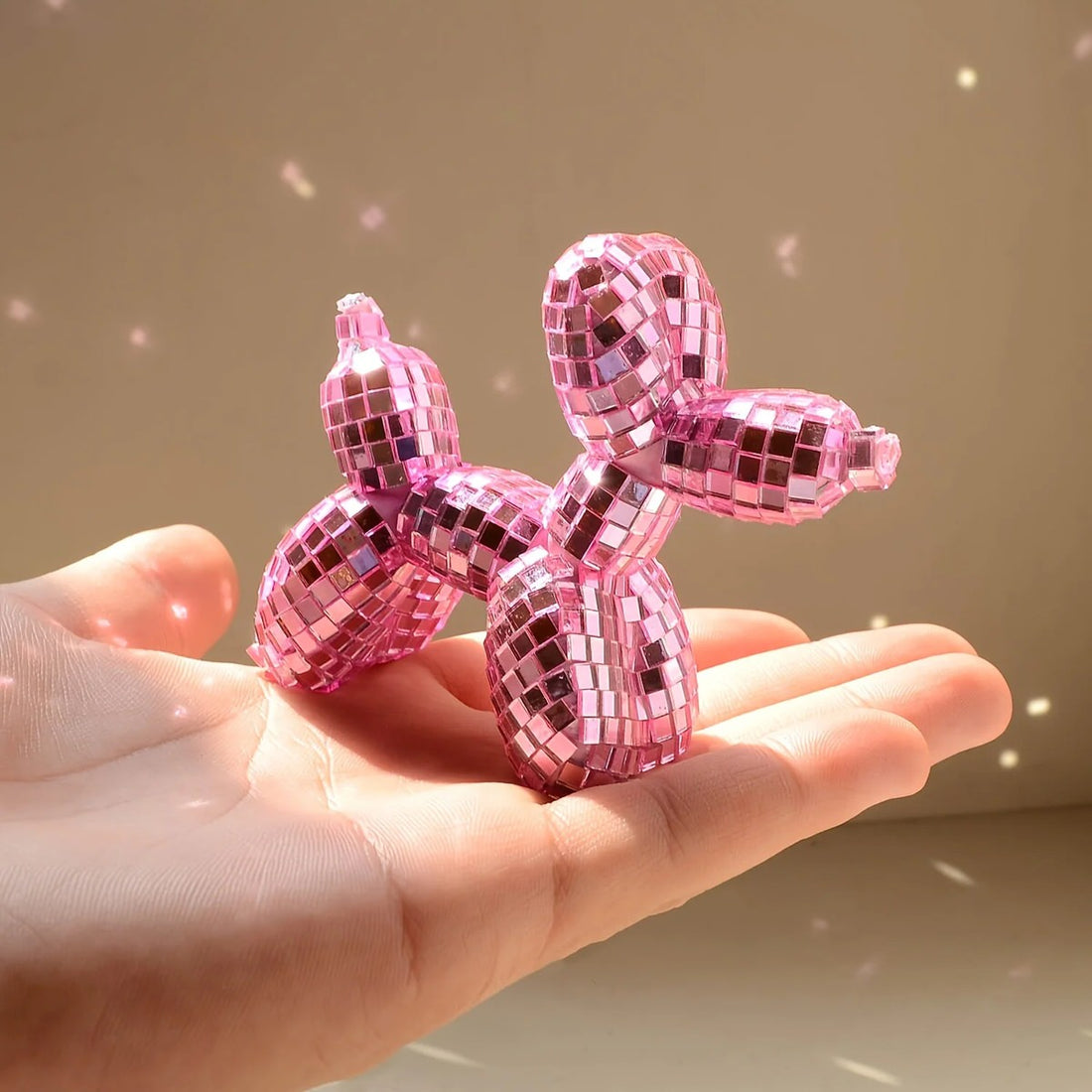 Small mirrored balloon dog decorative sculpture in silver and pink mosaic finish reflecting sunlight on a tabletop