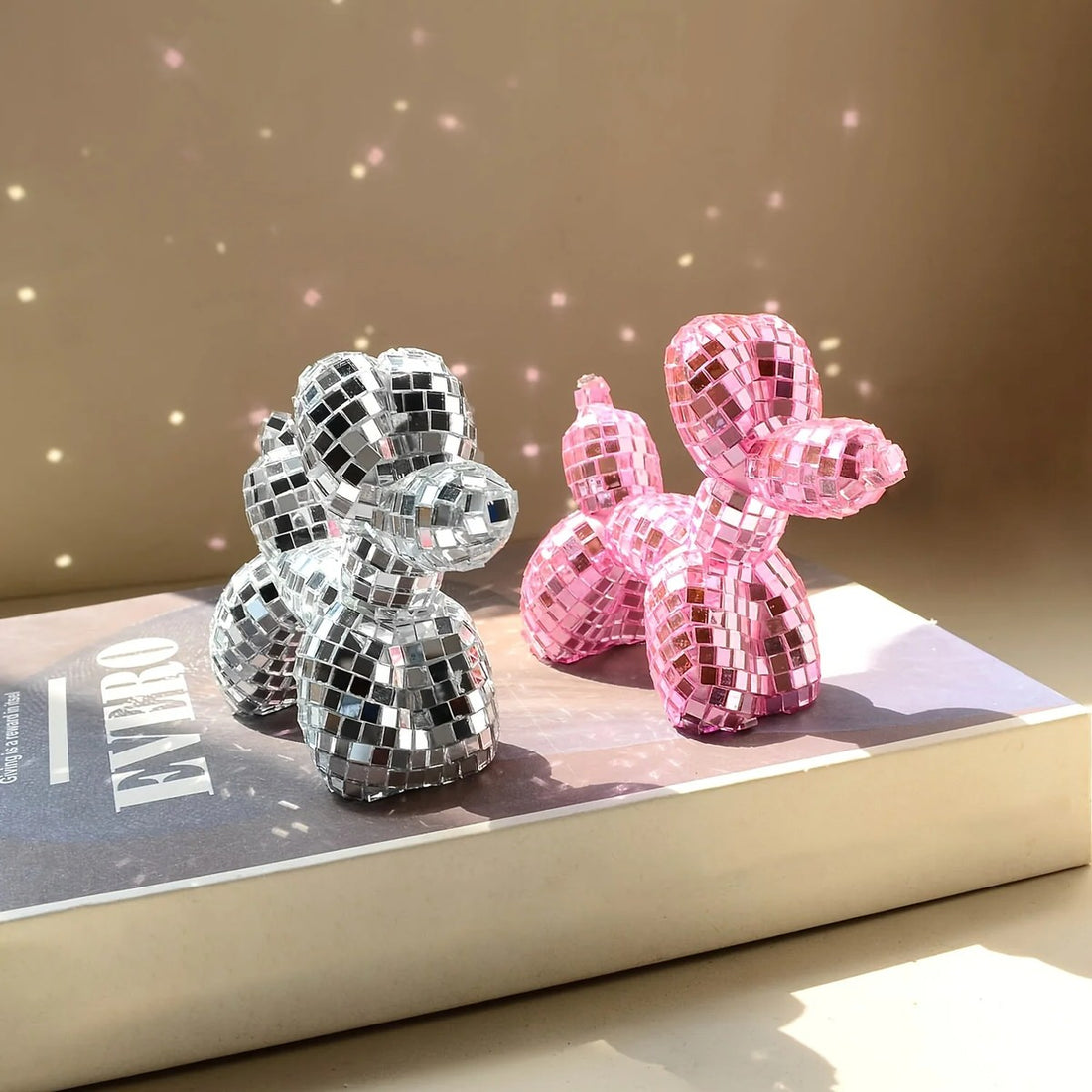 Small mirrored balloon dog decorative sculpture in silver and pink mosaic finish reflecting sunlight on a tabletop