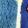 A tufted rug shaped like an arched window, displaying a blue sky with white clouds and a colorful bird on the sill
