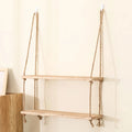 A rustic wooden shelf suspended by two thick natural-fiber rope hangers with knots