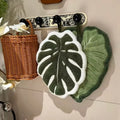 Leaf-shaped tufted hanging hand towel in green botanical designs with textured veins and hanging loop, shown in multiple tropical leaf styles and sizes.
