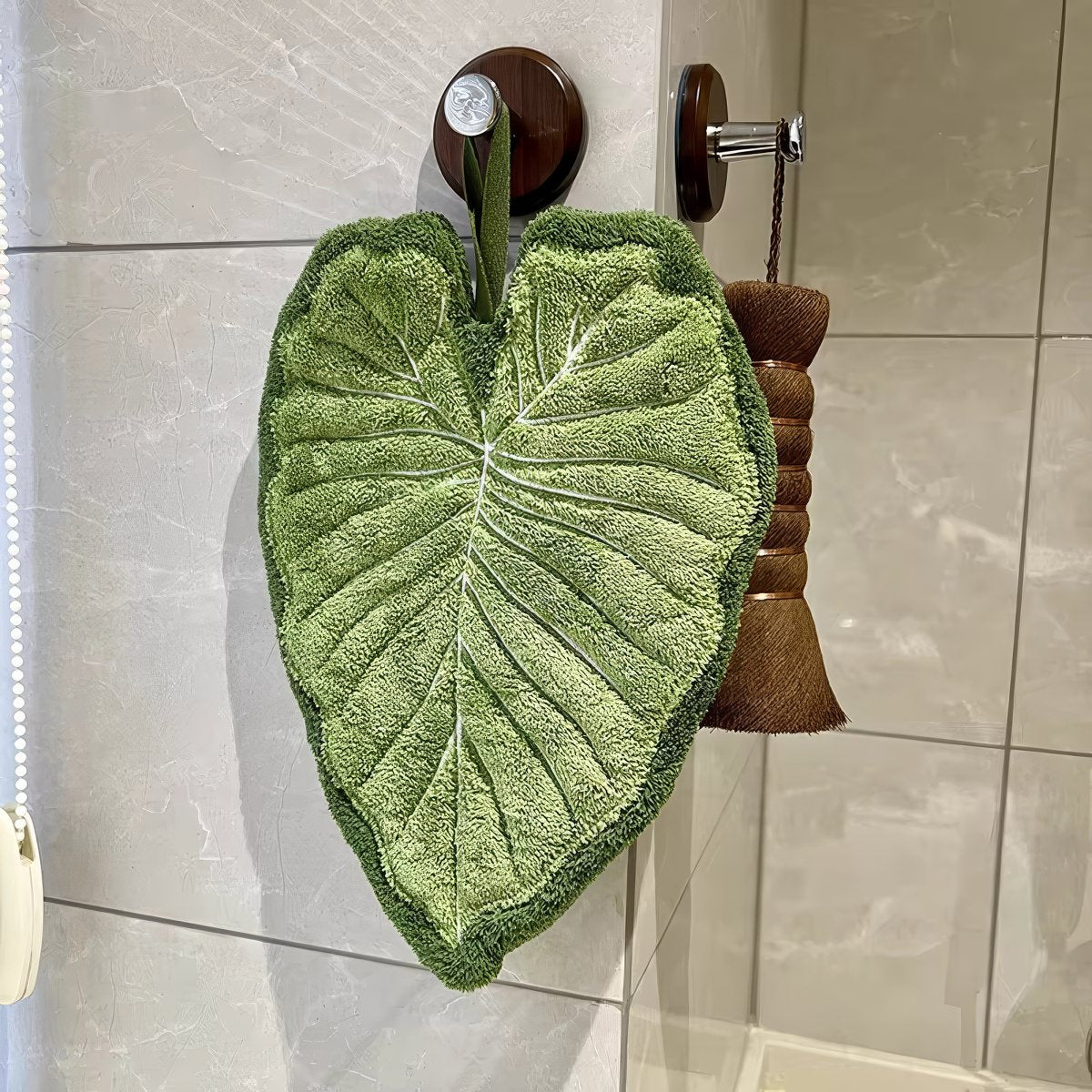 Leaf-shaped tufted hanging hand towel in green botanical designs with textured veins and hanging loop, shown in multiple tropical leaf styles and sizes.