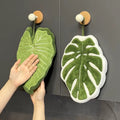 Leaf-shaped tufted hanging hand towel in green botanical designs with textured veins and hanging loop, shown in multiple tropical leaf styles and sizes.