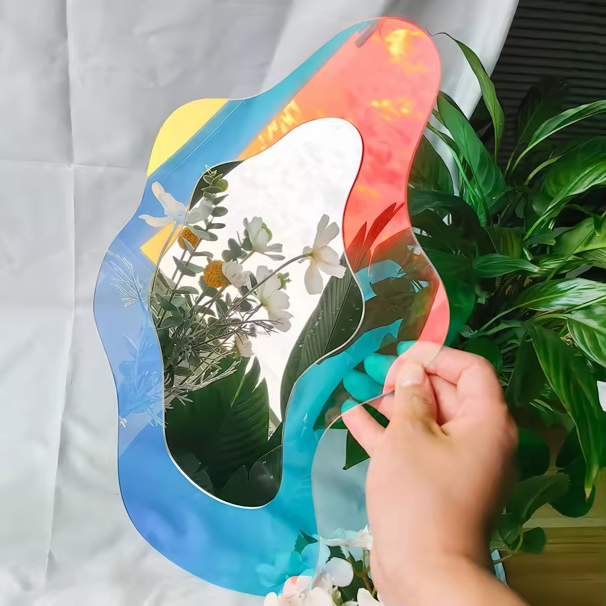 An abstract, wavy-edged acrylic mirror with a holographic iridescent finish that shifts between pink, purple, and light blue