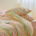 Pastel rainbow stripe bedding set with colorful lines on creamy background, paired with pink sheets.