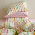 Pastel rainbow stripe bedding set with colorful lines on creamy background, paired with pink sheets.
