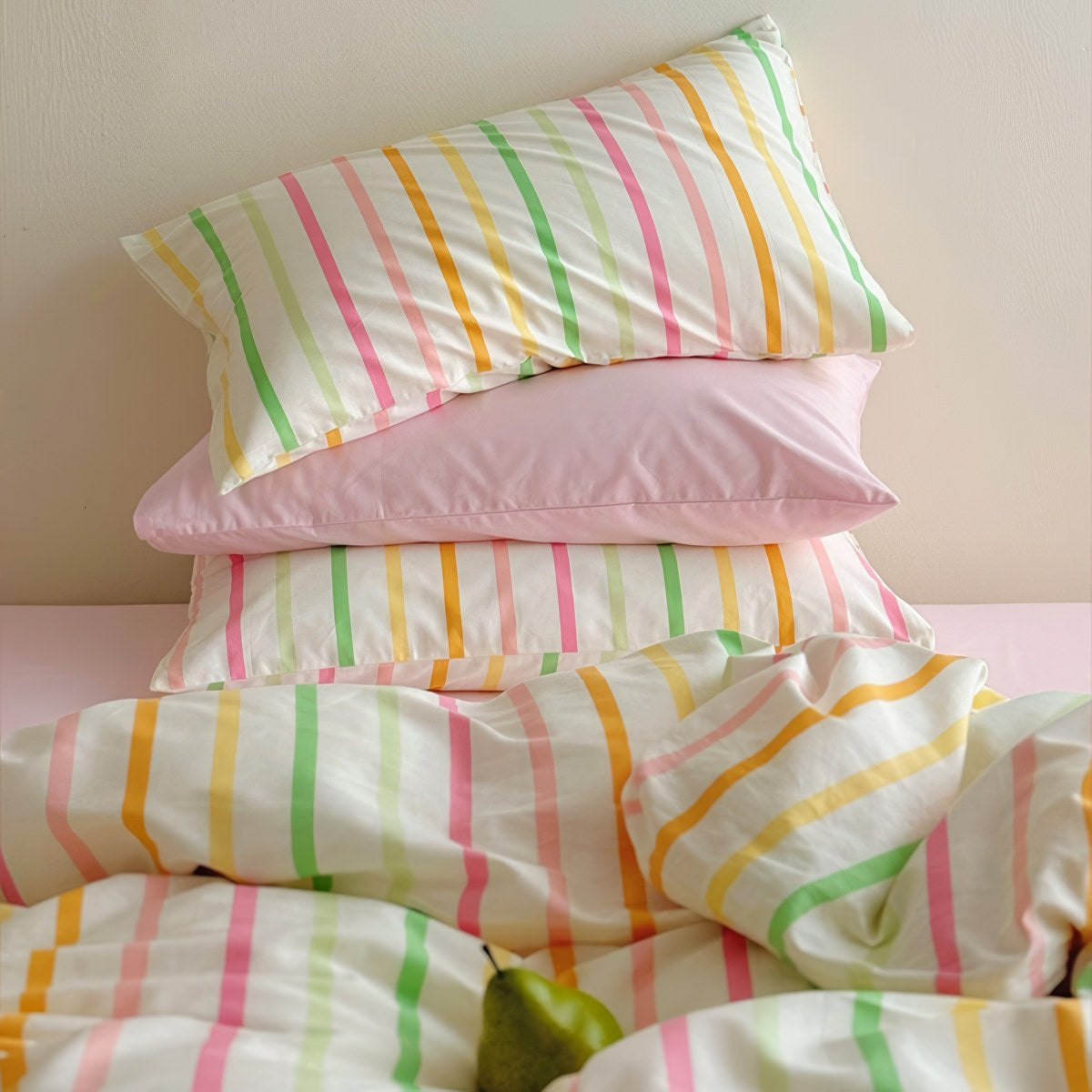 Pastel rainbow stripe bedding set with colorful lines on creamy background, paired with pink sheets.