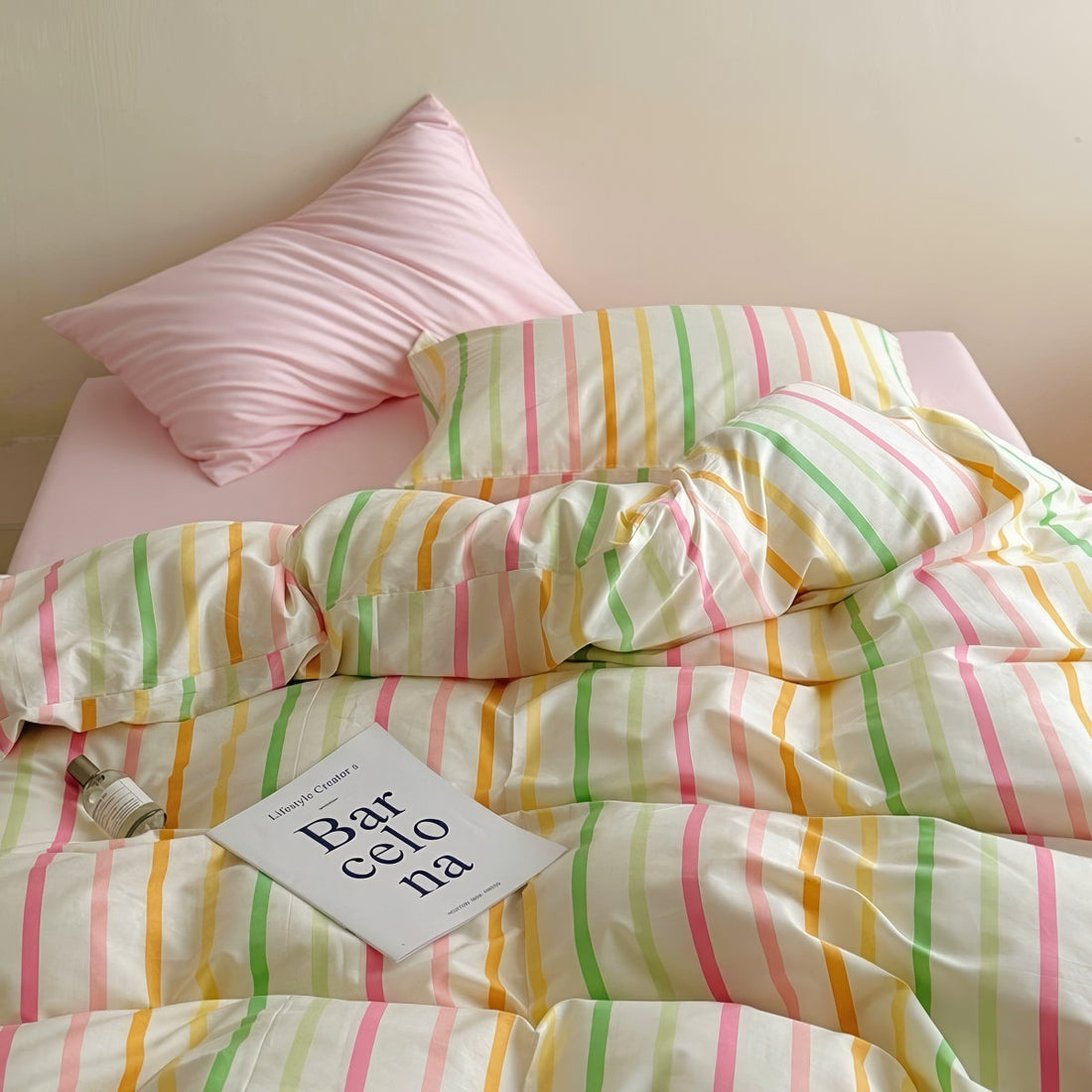 Pastel rainbow stripe bedding set with colorful lines on creamy background, paired with pink sheets.