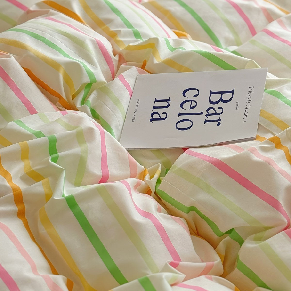 Pastel rainbow stripe bedding set with colorful lines on creamy background, paired with pink sheets.