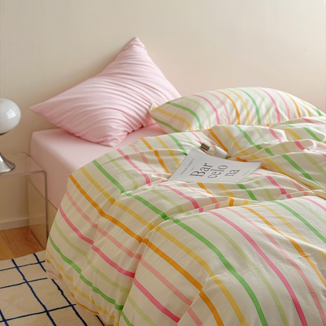 Pastel rainbow stripe bedding set with colorful lines on creamy background, paired with pink sheets.