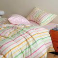 Pastel rainbow stripe bedding set with colorful lines on creamy background, paired with pink sheets.