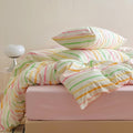 Pastel rainbow stripe bedding set with colorful lines on creamy background, paired with pink sheets.