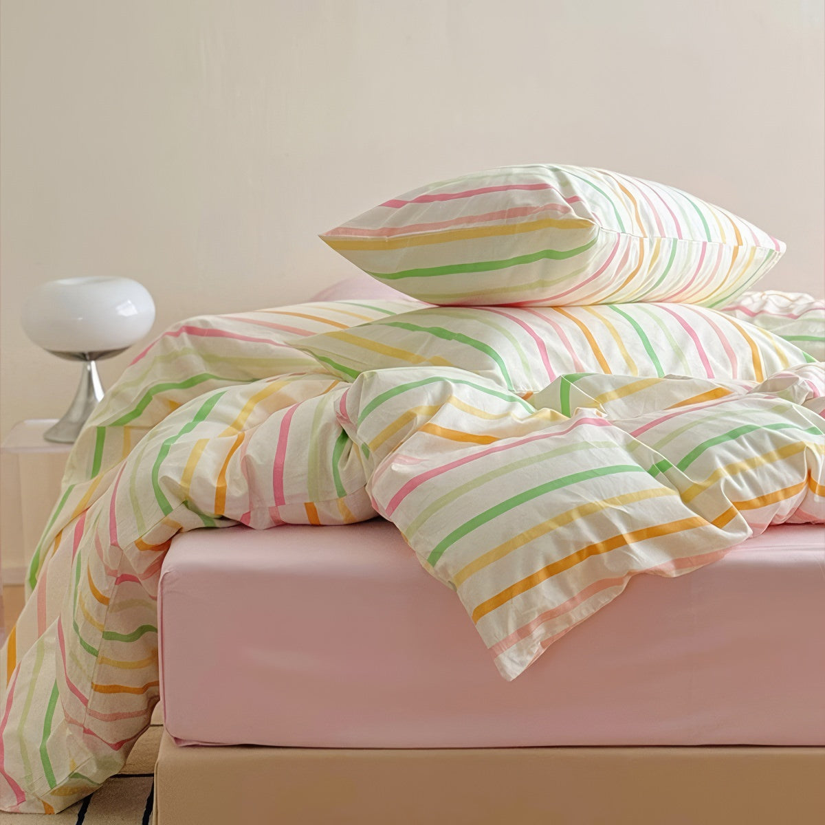 Pastel rainbow stripe bedding set with colorful lines on creamy background, paired with pink sheets.