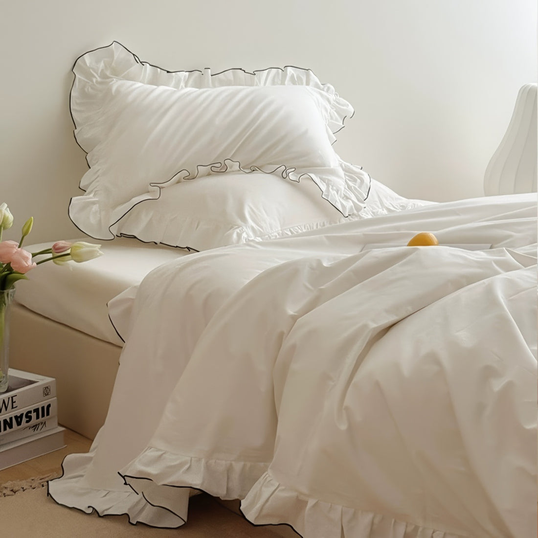 White bedding set with ruffled pillowcases trimmed in black piping, styled in a minimal bedroom.