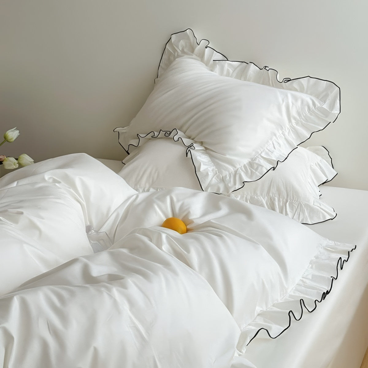 White bedding set with ruffled pillowcases trimmed in black piping, styled in a minimal bedroom.