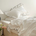 White bedding set with ruffled pillowcases trimmed in black piping, styled in a minimal bedroom.