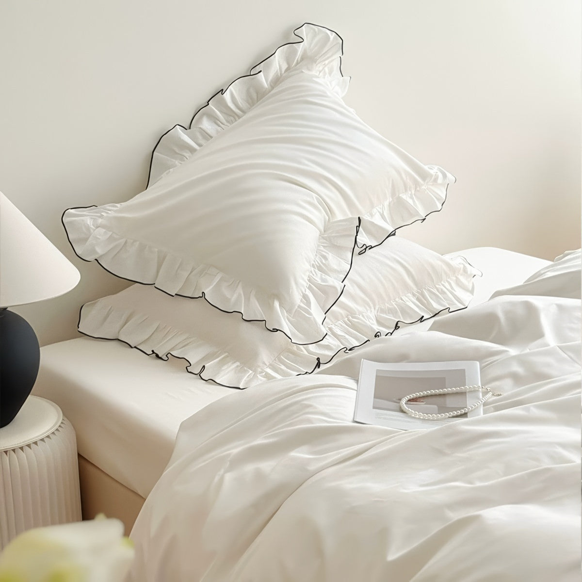 White bedding set with ruffled pillowcases trimmed in black piping, styled in a minimal bedroom.