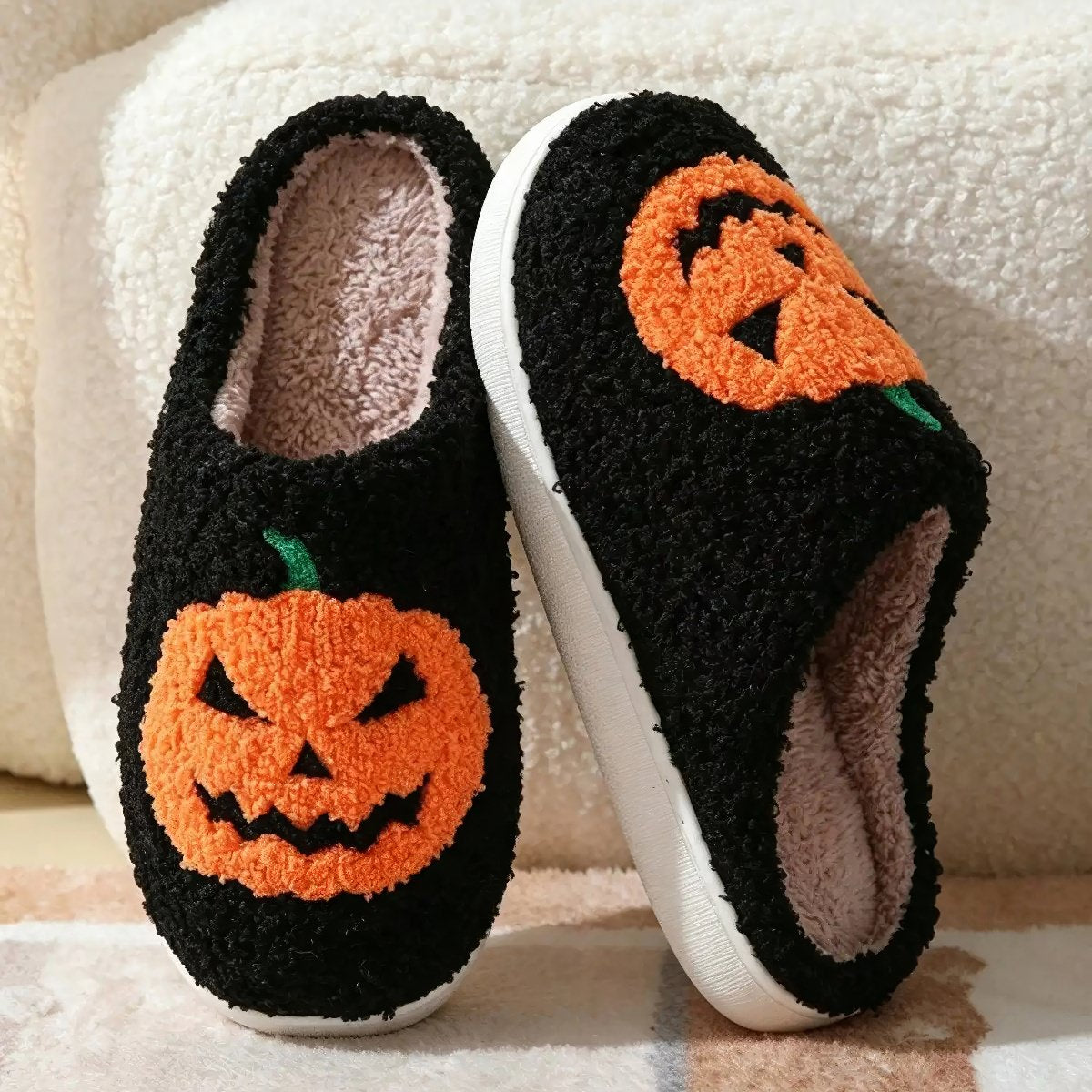 Plush Halloween slippers with embroidered jack-o’-lantern pumpkin in white and black.