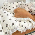 Cozy bedding set featuring white base with small black flowers with orange centers, bordered by white ruffles