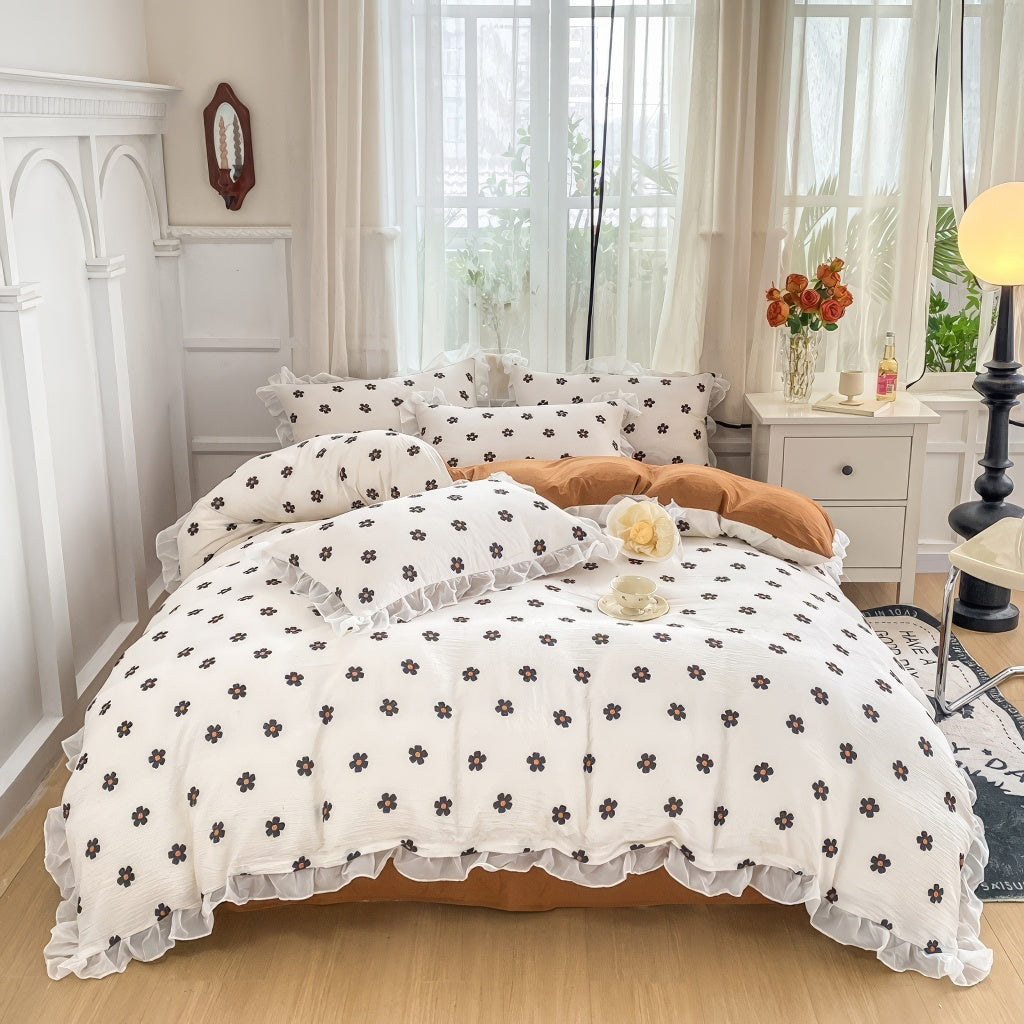 Cozy bedding set featuring white base with small black flowers with orange centers, bordered by white ruffles.