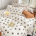 Cozy bedding set featuring white base with small black flowers with orange centers, bordered by white ruffles.