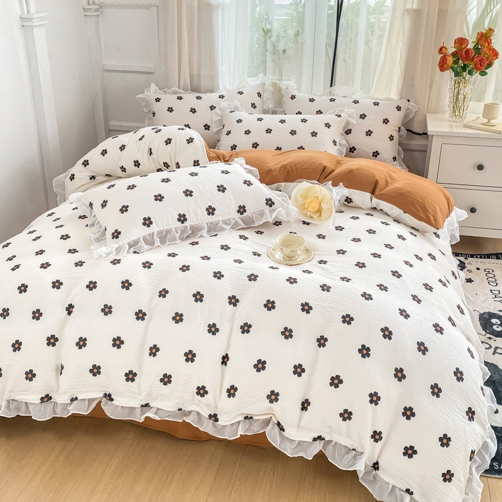 Cozy bedding set featuring white base with small black flowers with orange centers, bordered by white ruffles