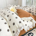 Cozy bedding set featuring white base with small black flowers with orange centers, bordered by white ruffles.