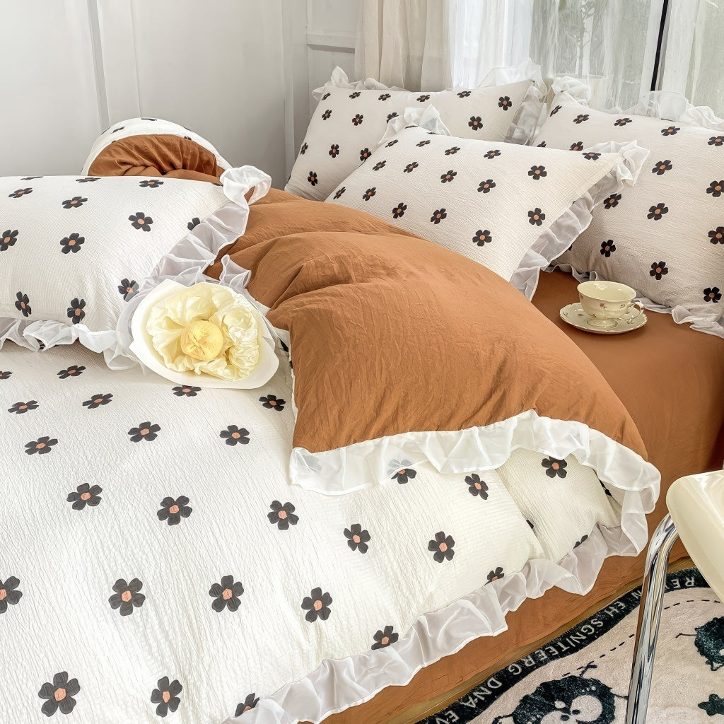 Cozy bedding set featuring white base with small black flowers with orange centers, bordered by white ruffles.